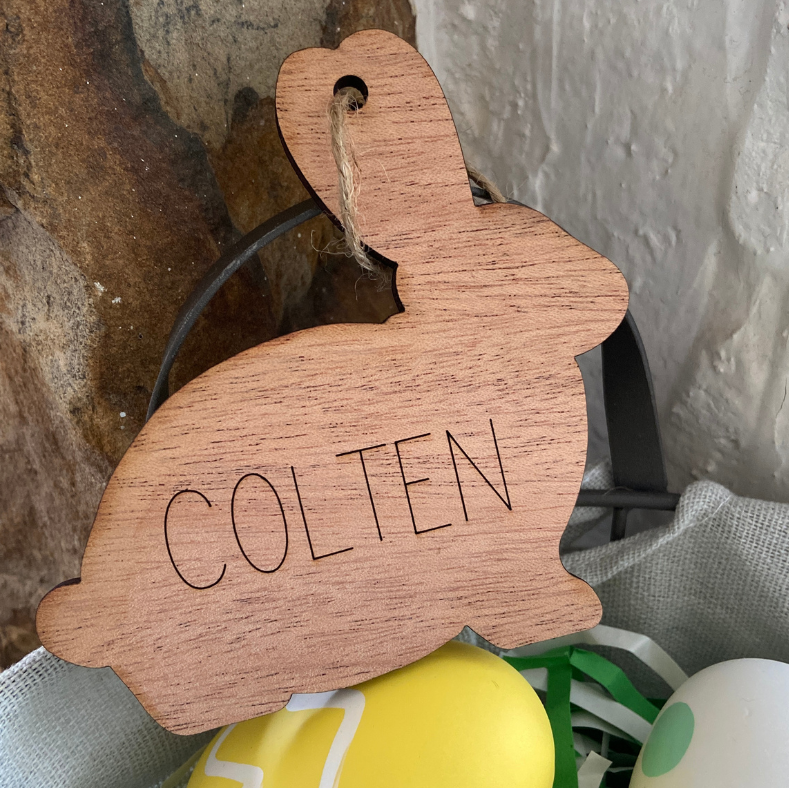 Wooden bunny-shaped tag with 'COLTEN' engraved, placed on Easter eggs.
