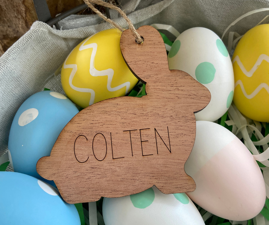 Wooden bunny-shaped ornament with 'COLTEN' engraved, surrounded by colorful Easter eggs.
