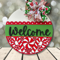 Decorative Christmas door hanger with gingerbread men, candy cane, and bow on a wooden surface.