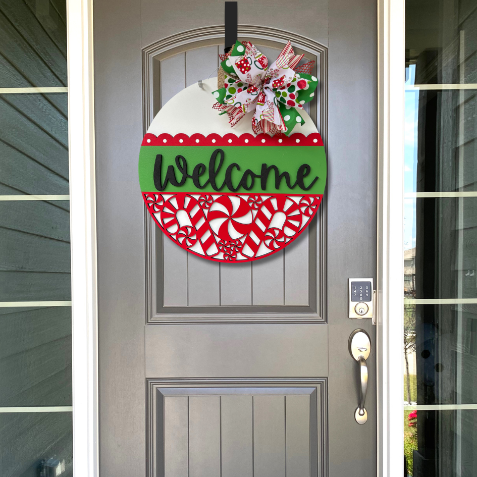Decorative door hanger with 'Welcome' text and candy cane pattern on a gray door.
