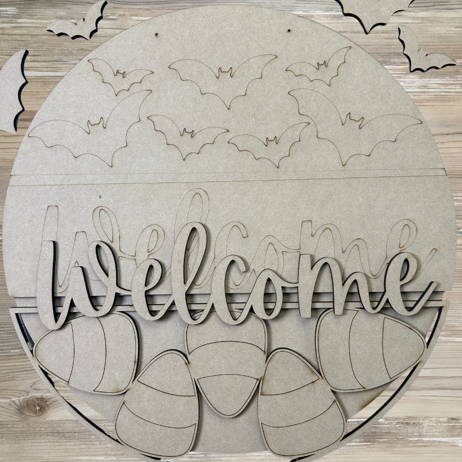 Round wooden cutout with 'Welcome' text and bat shapes on a wooden background