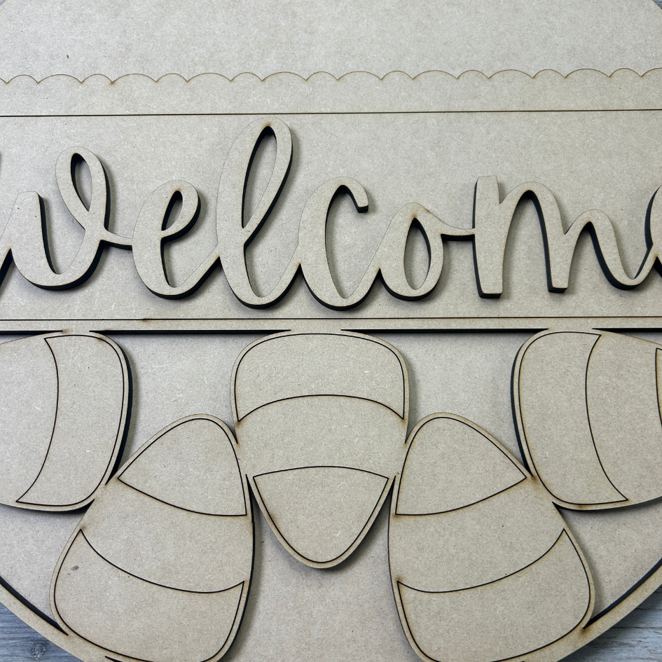 Wooden 'welcome' sign with candy corn designs on a light background