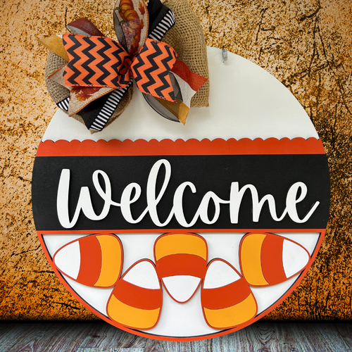Halloween-themed 'Welcome' sign with candy corn and a bow on a textured surface