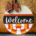 Halloween-themed 'Welcome' sign with candy corn and a bow on a textured surface.