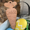 Wooden carrot-shaped tag with 'CHASE' engraved, placed among Easter eggs.
