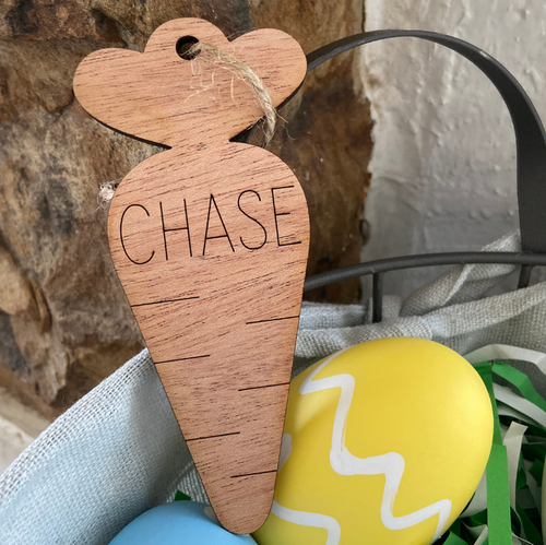 Wooden carrot-shaped tag with 'CHASE' engraved, placed among Easter eggs.