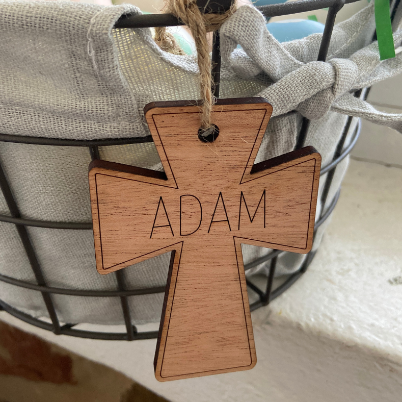 Wooden cross pendant with 'Adam' engraved, hanging from a string.