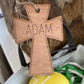 Wooden cross with 'ADAM' engraved, placed on a surface with decorative elements.