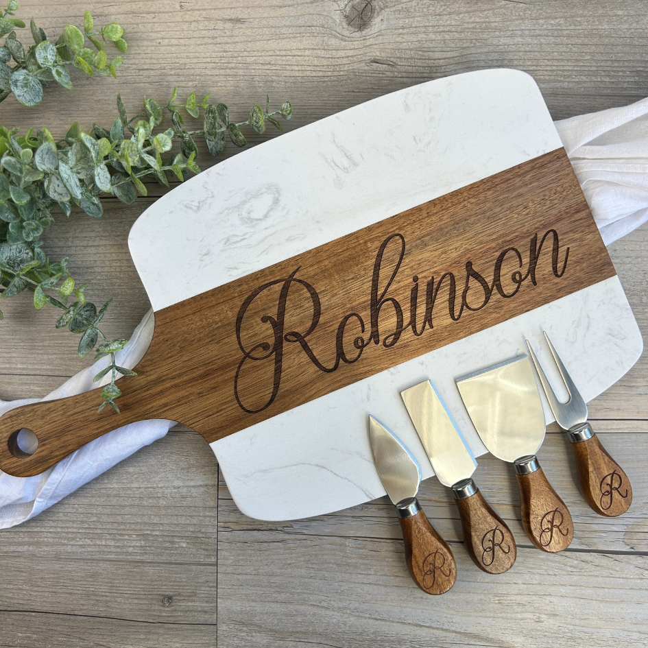 Wooden cutting board with engraved name 'Robinson' and matching cheese knives on a wooden surface.