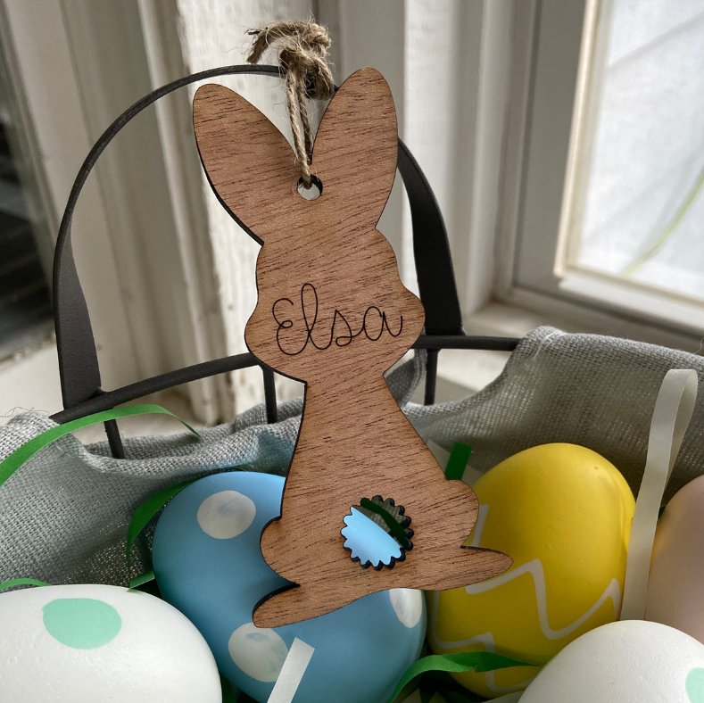Wooden bunny ornament with 'Elsa' engraved, surrounded by colorful Easter eggs.