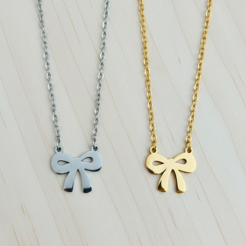 Two bow-shaped necklaces, one silver and one gold, on a light wooden surface.