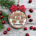Wooden ornament with names of grandchildren and a red bow, surrounded by cranberries and pine branches on a wooden surface.