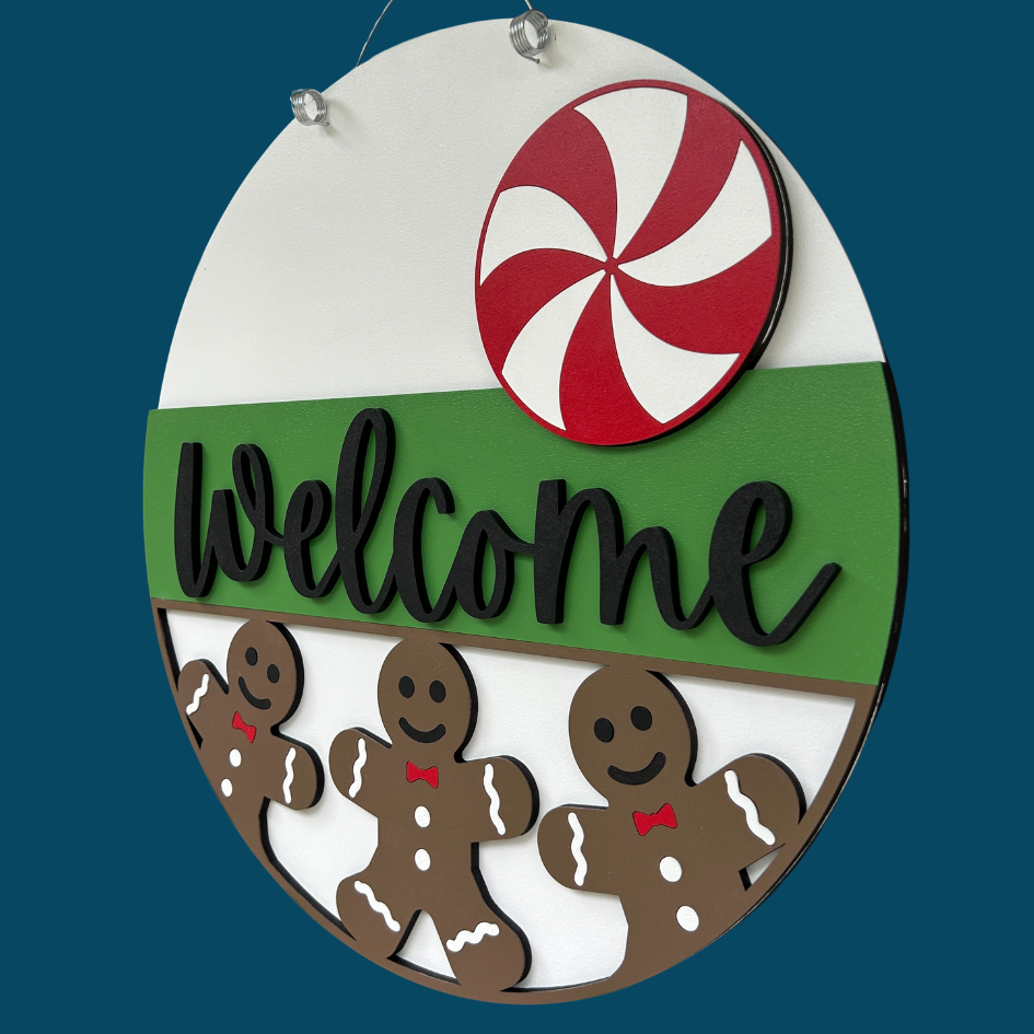 Decorative sign with gingerbread men, a peppermint candy, and the word 'Welcome' on a white background.