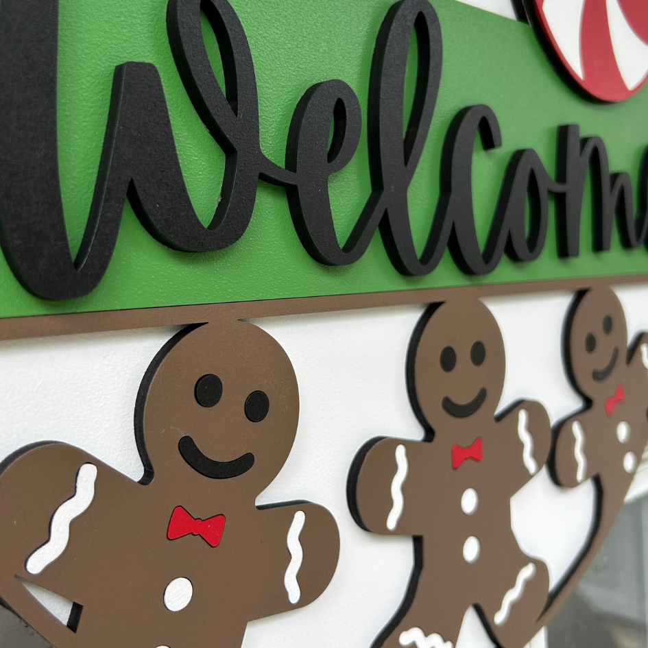Decorative sign with gingerbread men and the word 'Welcome' on a green background.