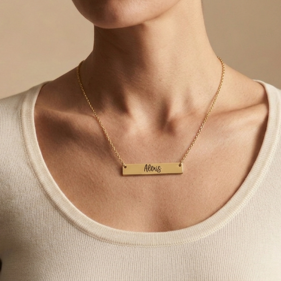Gold necklace with a name engraved on a bar pendant on a beige background