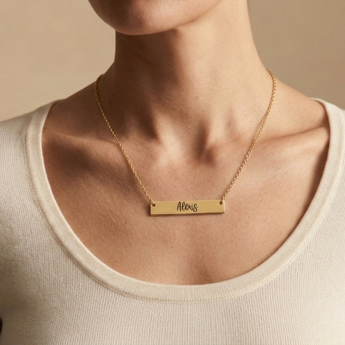 Gold necklace with a name engraved on a bar pendant on a beige background