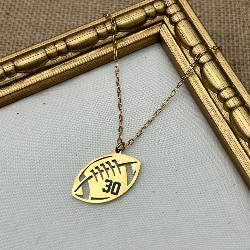 Gold necklace with a football-shaped pendant on a light gray background