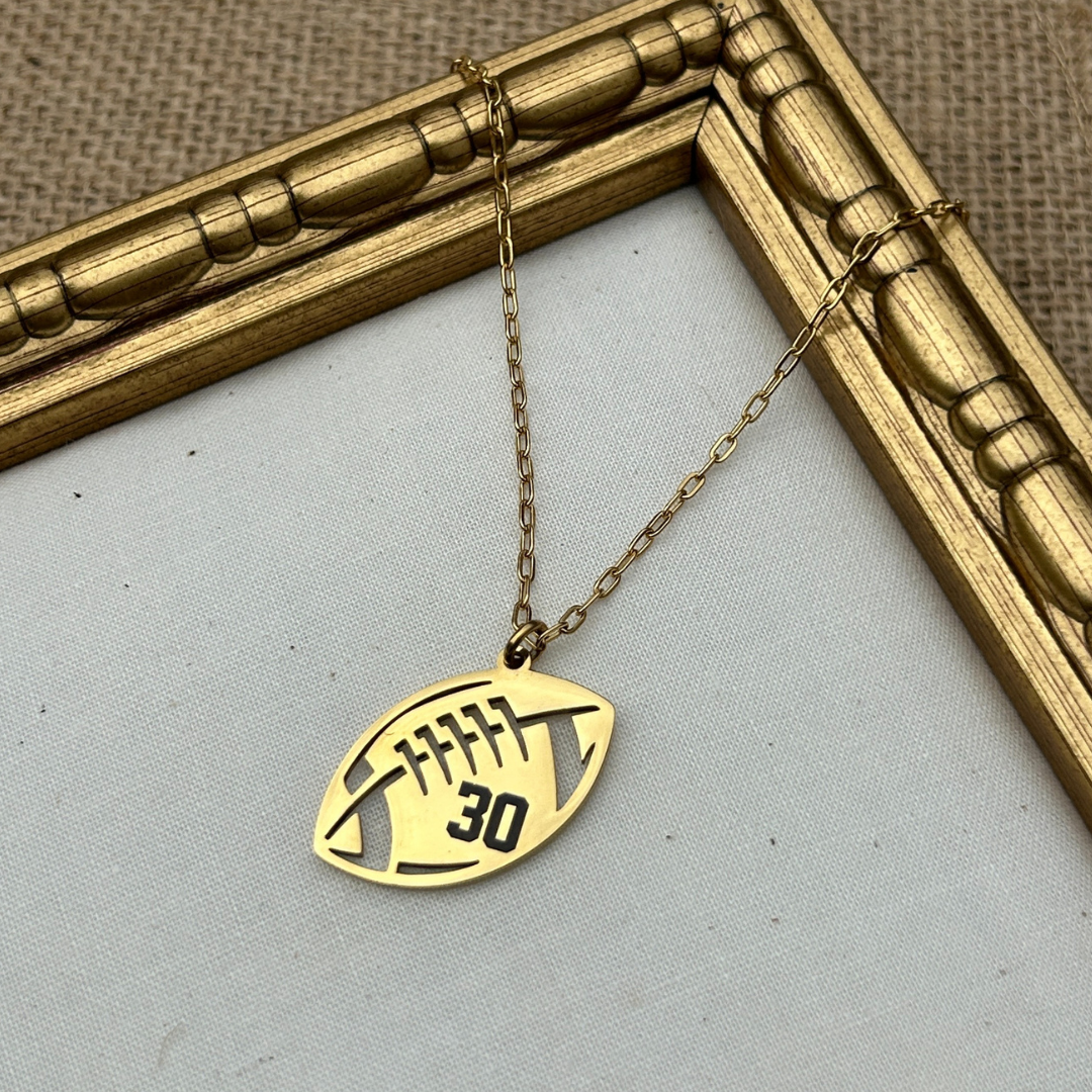 Gold necklace with a football-shaped pendant on a light gray background