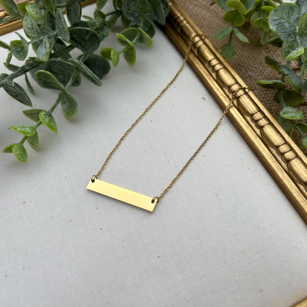 Gold necklace on a light gray surface with green leaves in the background