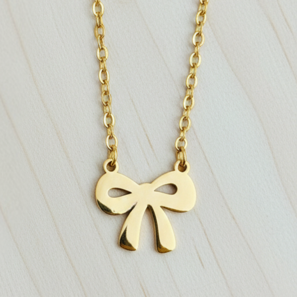Gold bow-shaped pendant necklace on a light wooden surface