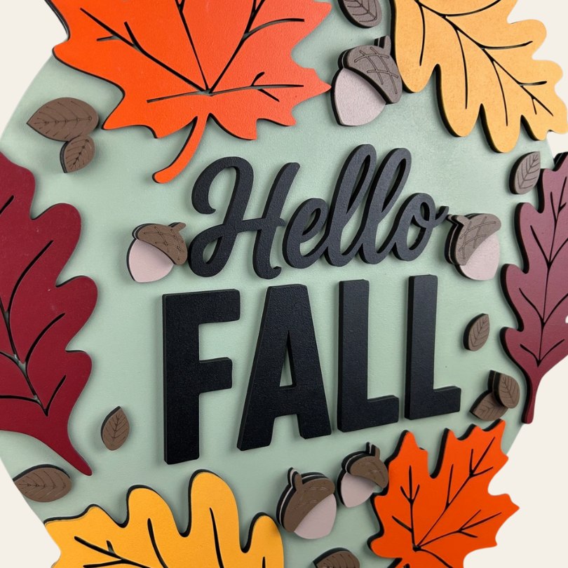 Decorative sign with 'Hello Fall' text surrounded by autumn leaves and acorns on a light green background.