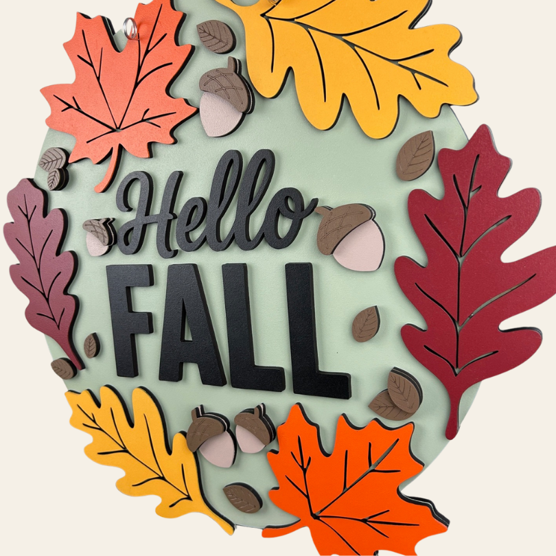 Decorative sign with autumn leaves and 'Hello Fall' text on a light green background