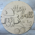 Circular wooden cutout with a face, bird, and 'Hey Yall' text on a wooden surface