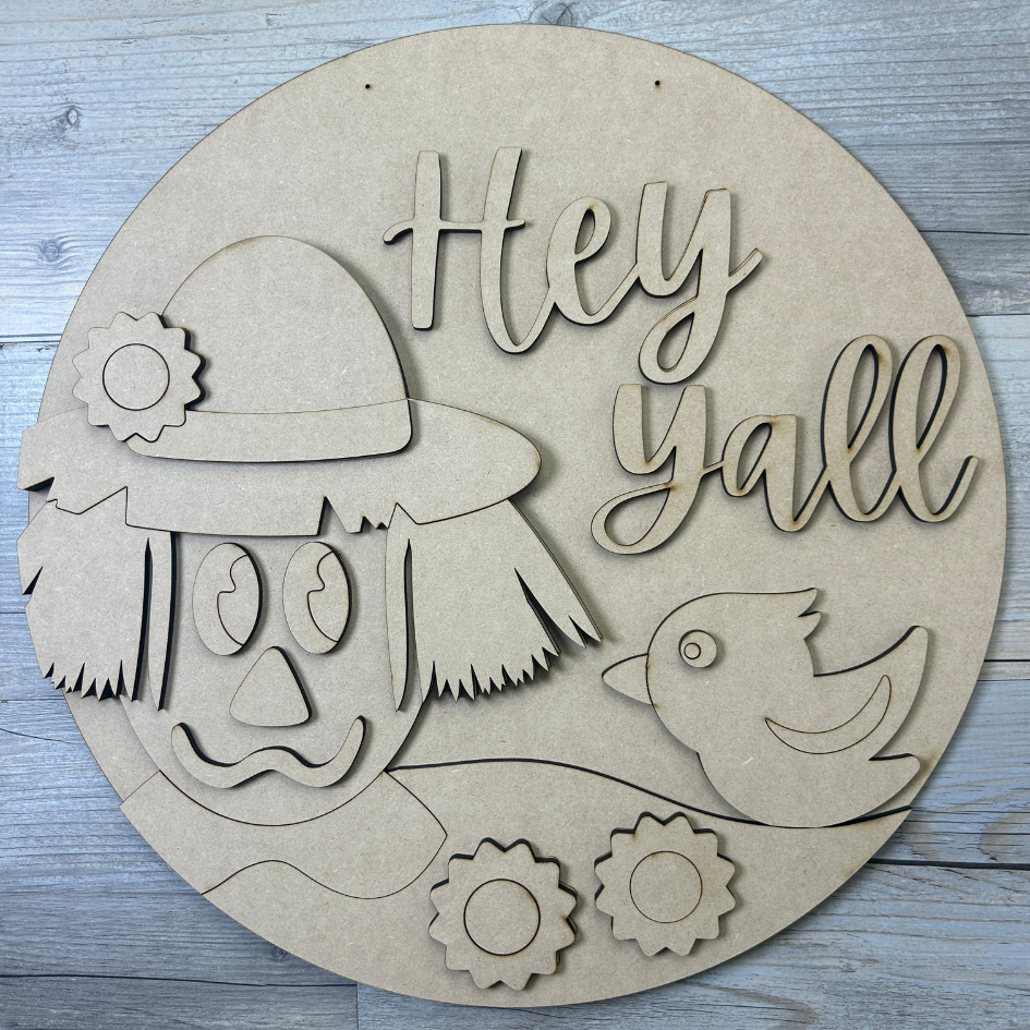 Circular wooden cutout with a face, bird, and 'Hey Yall' text on a wooden surface