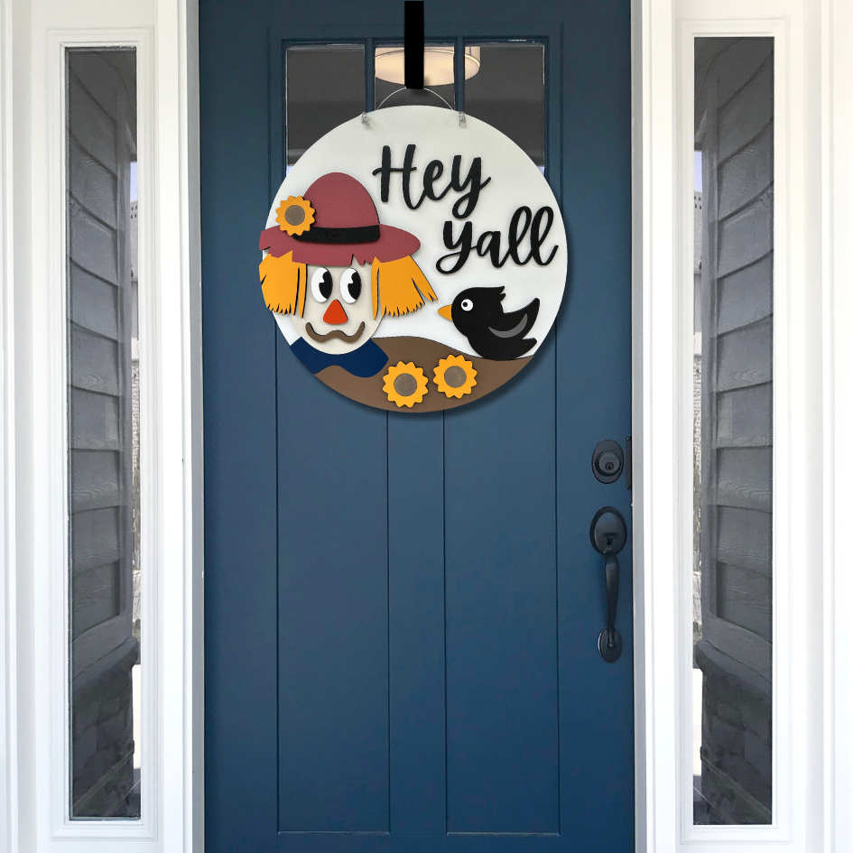 Decorative door hanger with scarecrow design and 'Hey Yall' text on a blue door.