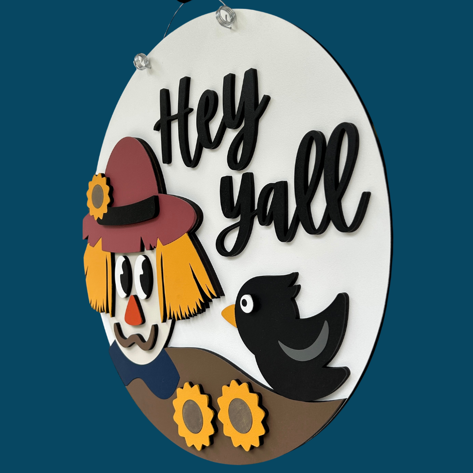 Decorative sign with scarecrow and crow illustration and 'Hey Yall' text on a white background.