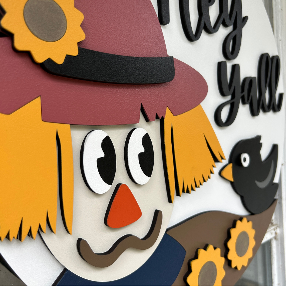 Decorative sign with a scarecrow face and text 'Hey Y'all' on a white background