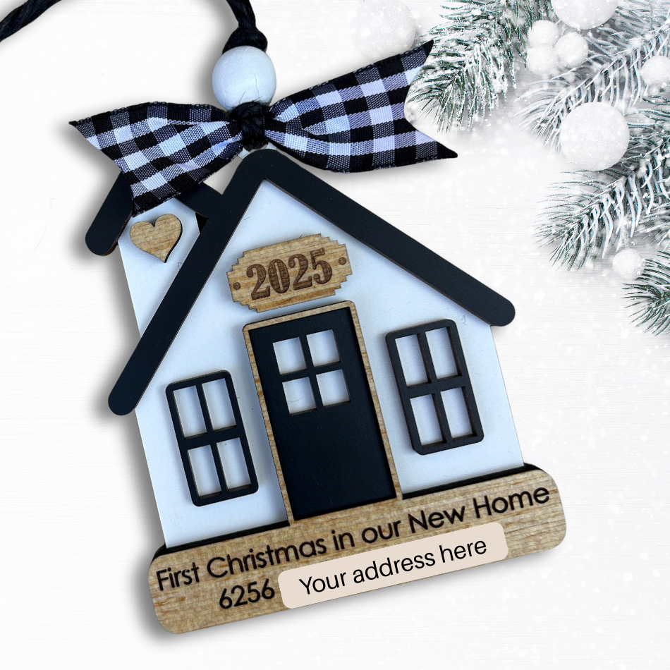House-shaped ornament with 'First Christmas in our New Home' text and address details, tied with a ribbon.