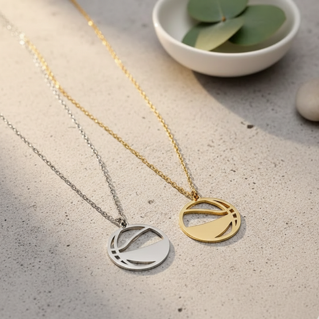 Two necklaces with circular basketball pendants on a textured surface with a small bowl of leaves.
