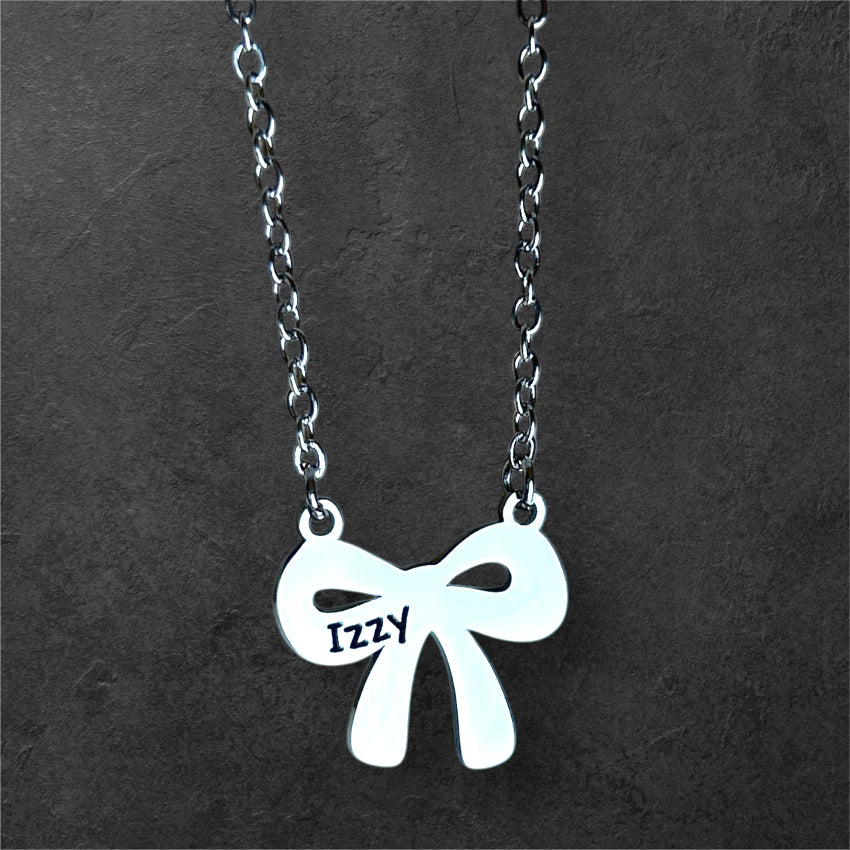 Silver bow-shaped pendant necklace with 'Izzy' engraving on a dark gray background