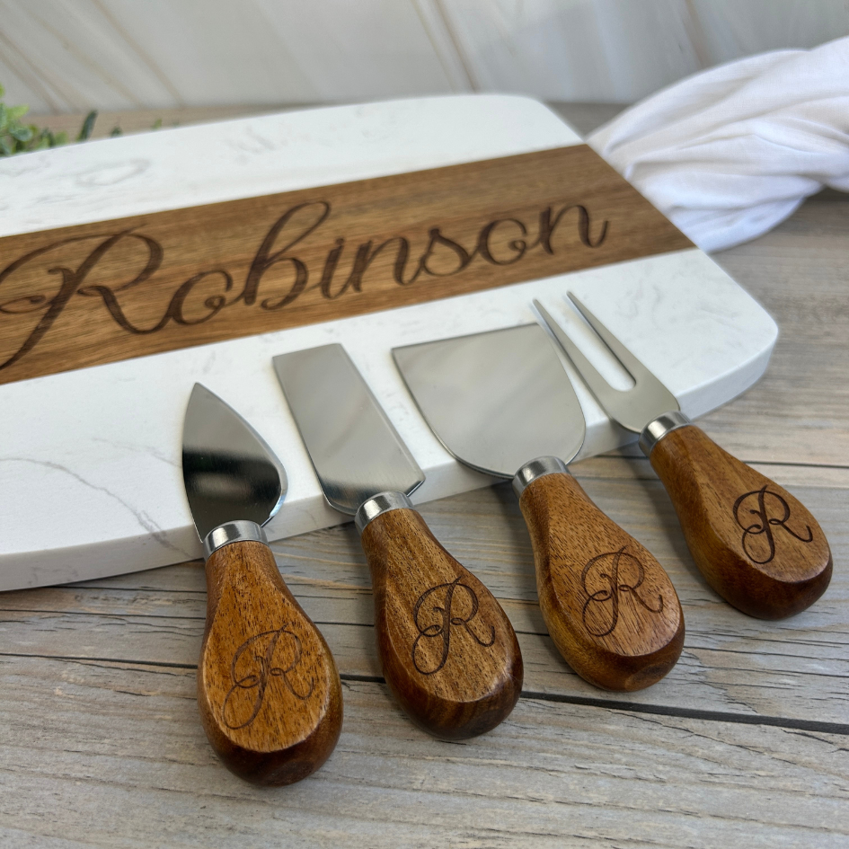 Set of four cheese knives with wooden handles and engraved 'R' on a cutting board with 'Robinson' engraving.