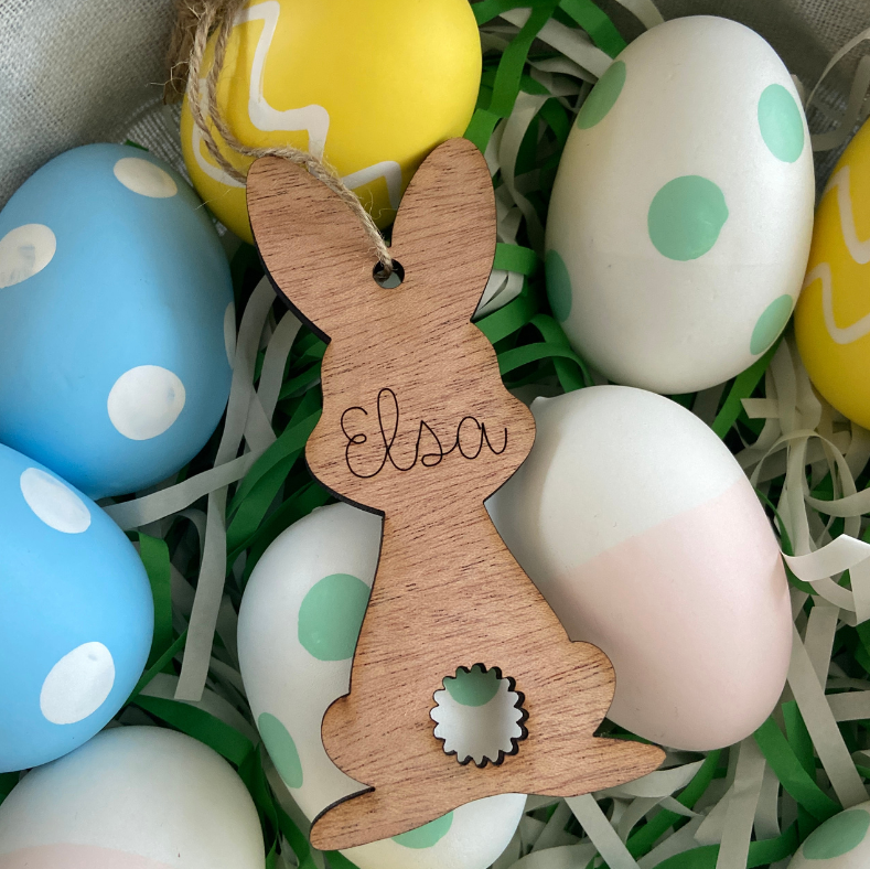 Wooden bunny ornament with 'Elsa' engraved, surrounded by colorful Easter eggs.