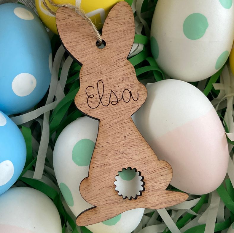 Wooden bunny ornament with 'Elsa' engraved, surrounded by colorful Easter eggs.