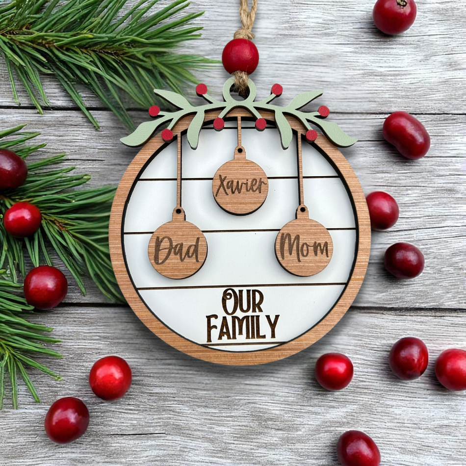 Decorative Christmas ornament with 'Dad', 'Mom', and 'Xavier' on a wooden circle, surrounded by cranberries and pine branches.