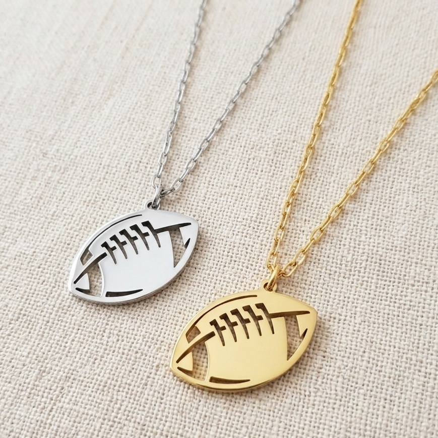 Two necklaces with football-shaped pendants, one gold and one silver, on a textured beige background.