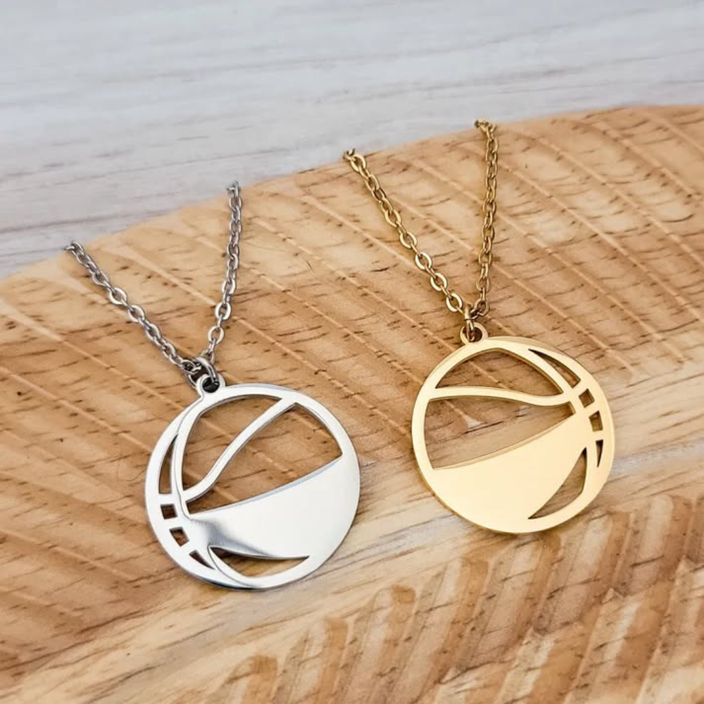 Two basketball necklaces, one silver and one gold, on a wooden surface.