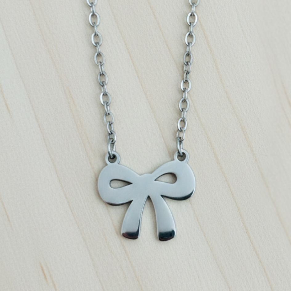 Silver bow-shaped pendant on a chain against a light wooden background