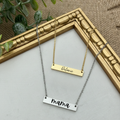 Two necklaces with engraved names hanging on a gold frame.