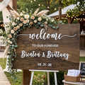 Wooden wedding sign with floral decorations and personalized text in an outdoor setting.
