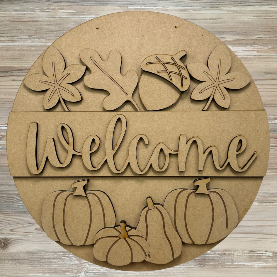 Round wooden sign with 'Welcome' text, pumpkins, and leaves on a wooden background