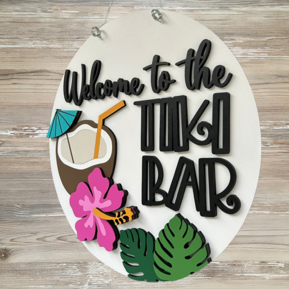Decorative sign with 'Welcome to the Tiki Bar' text, coconut, straw, and tropical leaves on a wooden background.