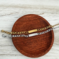Two gold and silver chain bracelets on a wooden disc with a light wood background
