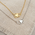 Two gold necklaces with geometric heart designs on a textured fabric background