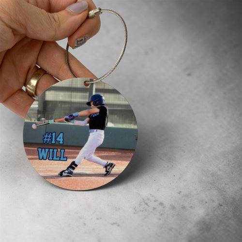 Round photo bag tag with a baseball player and text '#14 WILL' held by a hand on a gray background.