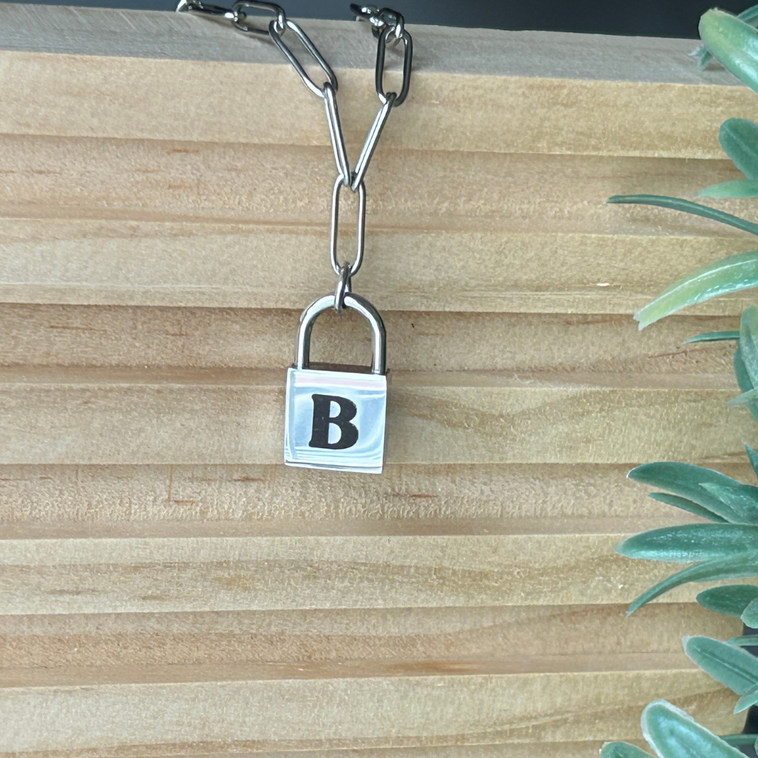 Close view of personalized silver chain bracelet with engraved B on a lock pendant on a wooden surface.
