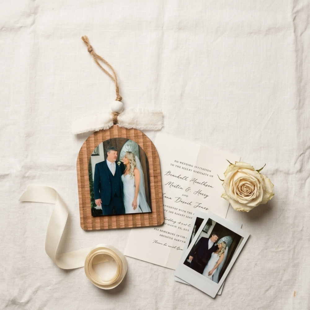 Wooden photo ornament with a father-daughter wedding picture, wedding invitation, and rose on a textured surface.